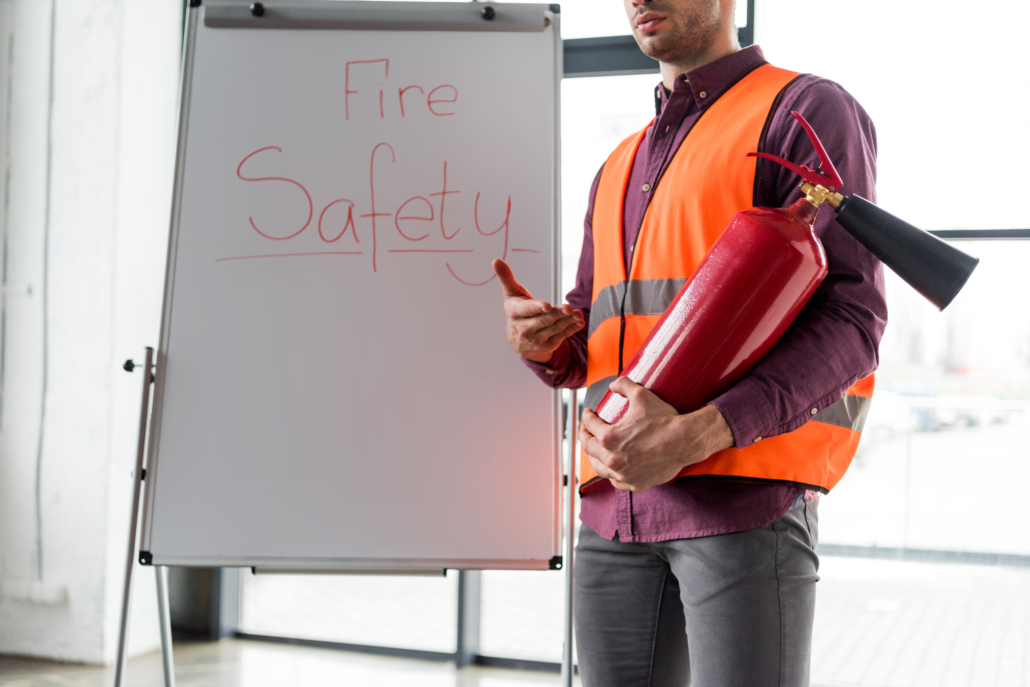 cropped view of fireman holding red extinguisher while standing near white board with fire safety